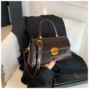 Dettaglio borsa in pelle lucida marrone scuro con chiusura dorata e tracolla sottile
