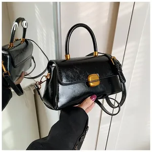 Dettaglio di una borsa in pelle nera lucida con una chiusura metallica quadrata dorata