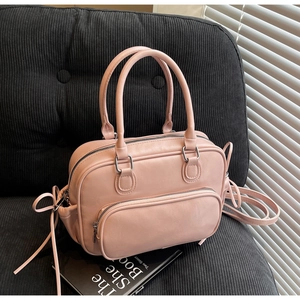 Detail of pink PU leather bowling bag with zipper pocket and dual handles on black sofa