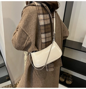 Detailansicht einer cremefarbenen Baguette-Tasche mit Silberkette zum Mantel