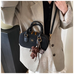 Close-up of black retro Boston bag with plush bear charm and mini book accessory