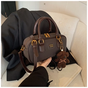 Close-up of a vintage dark brown Boston bag with a cute teddy bear charm on a sofa
