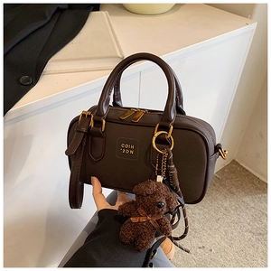 Detail of dark brown matte Boston bag with top handles and a cute plush bear pendant