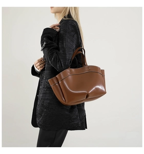 Detail of a large brown leather tote bag with vertical stitching and side wing pockets
