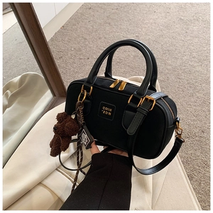 Detail of black boston bag with gold hardware and a cute brown plush bear charm accessory