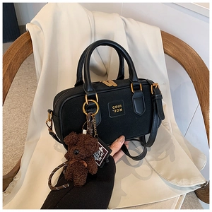 Detail of black leather handbag with gold zippers, teddy bear and holy bible pendants