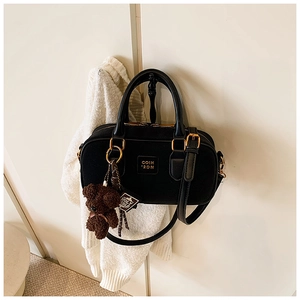 Detail of black bowling handbag with gold hardware and a cute brown bear charm