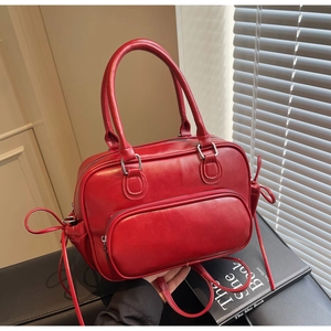 Detail of red leather bowling bag featuring decorative side bows and front zip pocket