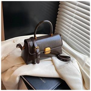 Dettaglio della borsa a mano vintage in pelle marrone con fibbia dorata su blazer bianco