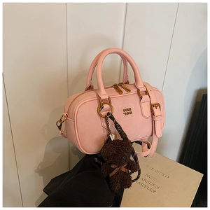 Detail of pink faux leather boston bag with gold hardware and brown teddy bear charm