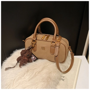 Close-up of brown Boston bag with golden zipper and a cute plush teddy bear charm
