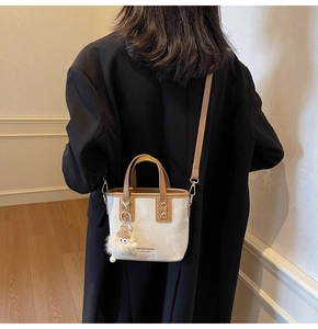 Detail einer beigen Beuteltasche mit braunem Rand und einem süßen Plüsch-Anhänger