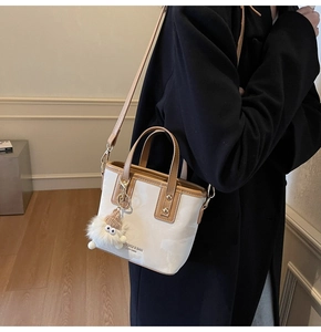 Detailansicht der creme-braunen Beuteltasche mit Plüschanhänger und Markenlogo