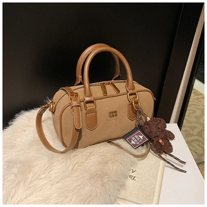 Detail view of khaki leather Boston bag with gold hardware and plush bear charm