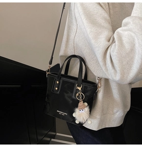 Detail einer schwarzen Lederbeuteltasche mit Goldbeschlägen und weißem Plüsch-Anhänger