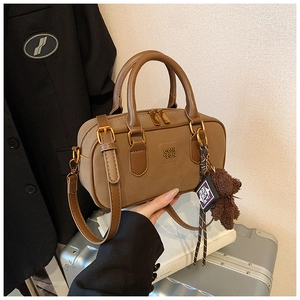 Close-up of tan leather Boston bag with embossed logo and plush bear accessory