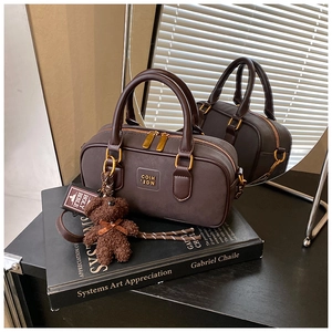Detail of dark brown leather Boston bag with gold logo, plush bear charm and woven strap