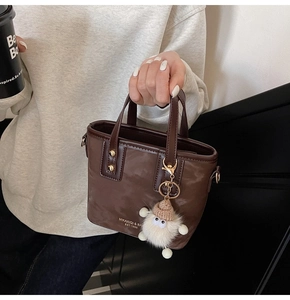 Nahaufnahme der braunen Eimer-Tasche aus Kunstleder mit goldenen Details und Lamm-Anhänger