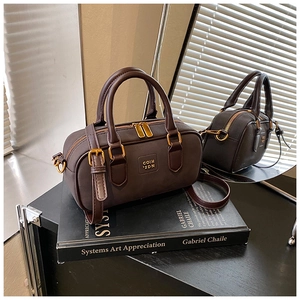 Detailed close-up of dark brown leather Boston bag with gold hardware on a book