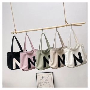 Selection of five canvas tote bags in various colors hanging from a wooden rack