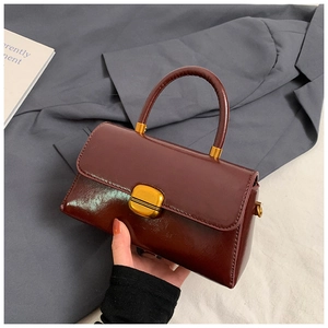 Dettaglio mini borsa in pelle bordeaux con fibbia dorata e manico su tessuto grigio