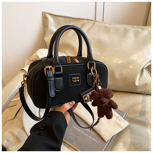 Detail of black Boston bag with dual handles and a brown plush teddy bear charm