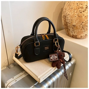 Detail of black leather boston bag with golden hardware and cute bear pendant charm