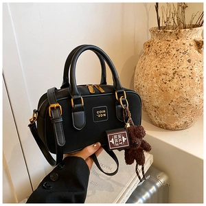 Detail of vintage black Boston bag with gold hardware and plush bear charm on a desk