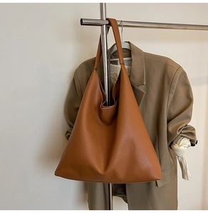 Detail view of large brown pebble leather tote bag with elegant draped top and wide strap