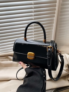 Borsa a mano vintage nera con chiusura dorata indossata da una donna in blazer