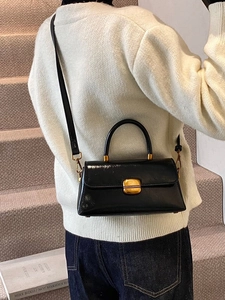 Borsa a mano retrò in pelle nera con fibbia dorata indossata da una modella in un interno moderno