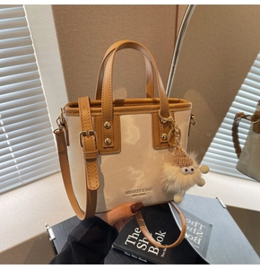 Detail der cremefarbenen Beuteltasche mit braunem Lederbesatz und Plüsch-Anhänger