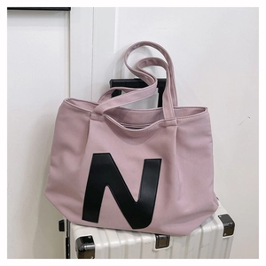 Detailed view of pink canvas tote bag with a large black N letter on a white suitcase