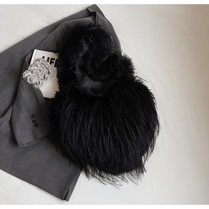 Détail d'un sac cœur en fausse fourrure noire avec franges sur une veste grise