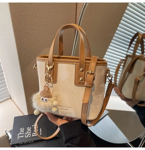 Detail der cremefarbenen Beuteltasche mit braunem Rand, Logo-Prägung und Plüsch-Anhänger