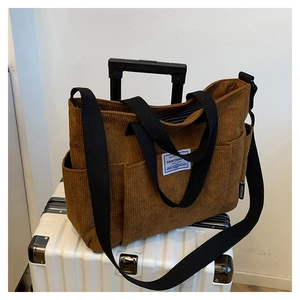 Detail of brown corduroy tote bag with adjustable black strap on white suitcase