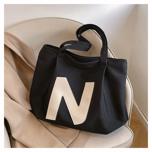 Detail of black canvas tote bag with cream N logo leaning on a white chair in a home setting