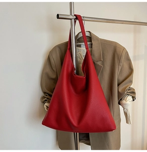 Detailed view of red pebble leather tote bag with wide strap hanging on clothes rack
