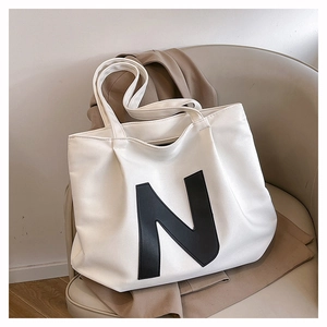 Minimalist white canvas tote bag with bold black letter N detail on a stylish sofa chair