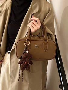 Retro dark brown boston bag with teddy bear pendant shown in a stylish hand-held pose