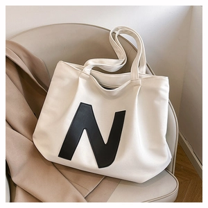 Detail of a large white tote bag with a bold black N logo placed on a grey chair