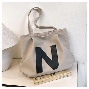 Detail of a beige canvas tote bag featuring a black N logo and long dual handles