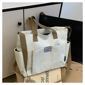 Detail view of corduroy tote bag with multiple front pockets and brown webbing straps