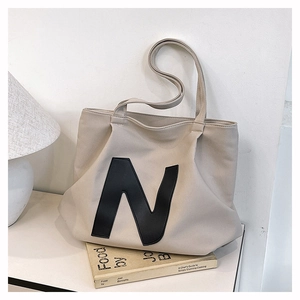 Close-up of beige canvas tote bag featuring a large black letter N patch and leather detail