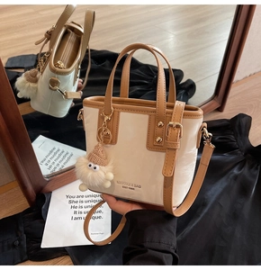 Detailansicht der cremefarbenen Beuteltasche mit braunem Rand und Plüsch-Charm