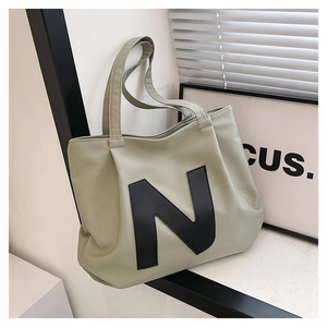 Detailed texture of sage green canvas tote bag featuring a black leather 'N' patch logo