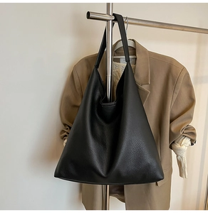 Detail of black pebbled leather tote bag hanging with minimalist integrated shoulder strap