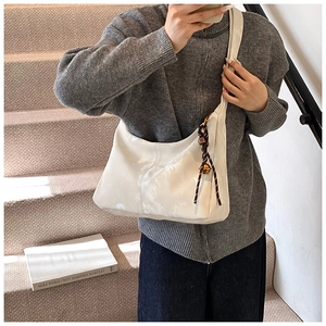 White patent leather hobo bag with woven charm shown on model in cozy indoor setting