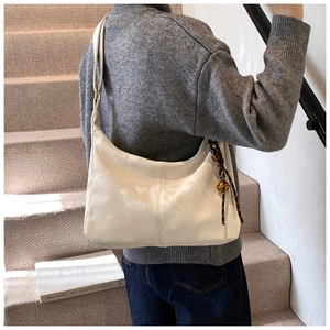 Detail of white soft leather hobo bag with woven knot and gold bell charm on a model