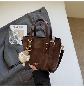 Detailaufnahme der braunen Handtasche aus mattem Leder mit Griffen und Fellanhänger